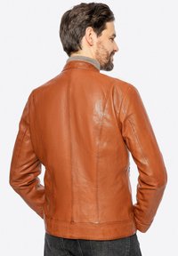 Giacca di pelle marrone con una texture liscia, design attillato, colletto alto e cuciture ben definite lungo la schiena e le spalle.