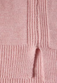 Tejido de punto rosa claro con textura acanalada y un patrón de puntos alternos, con un pequeño detalle de corte en un lado.