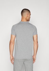 Grå kortermet polo-shirt laget av mykt stoff, med en rund hals og en litt slim fit-design, vist fra baksiden.