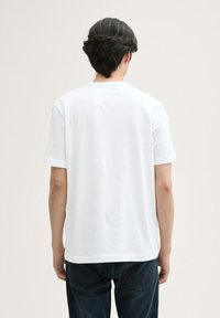 Hvid T-shirt med kortærmer lavet af bomuld, med en klassisk rund hals og en afslappet pasform. Båret med mørkeblå denimjeans.