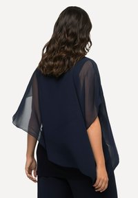 Marineblaues Chiffon-Cape mit weiten, fließenden Ärmeln. Leichtes und halbtransparentes Material, das über einem dunklen Top geschichtet ist und einen lockeren Sitz bietet.