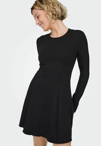 Czarna sukienka z długim rękawem, dopasowaną górą i rozkloszowanym dołem. Gładka faktura i subtelne detale szwów. Okrągły dekolt, długość do kolan.