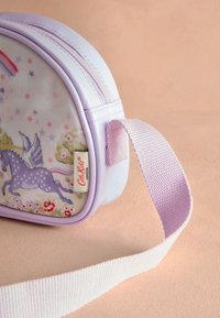 Liten pastelllila väska med dragkedja, dekorerad med en lila enhörning med vingar, regnbåge, stjärnor och blommönster, samt ett matchande tygband.