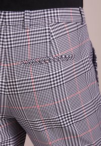 Pantaloni a scacchi bianco e nero caratterizzati da un tessuto testurizzato, linee di accentuazione rosse e una tasca posteriore con dettaglio di design intrecciato.