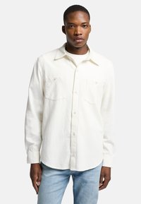 Camicia bianca con bottoni in cotone, caratterizzata da un colletto, due tasche sul petto e maniche lunghe con polsini abbottonati. Design semplice e monocolore.