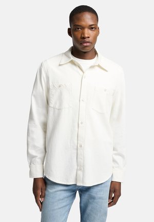 Chemise blanche à boutons en coton, dotée d'un col, de deux poches poitrine et de manches longues avec des poignets boutonnés. Design simple et uni.