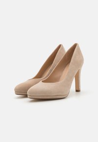 Escarpins en daim beige avec un bout arrondi, un décolleté bas et un talon stiletto fin, présentant une texture lisse et des détails minimalistes.