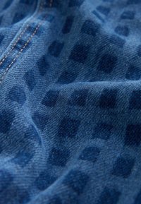 Modra denim tkanina z diskretnim temnim diamantnim vzorcem, vidnimi šivi in raznolikimi teksturami zaradi gub in zvijanja.