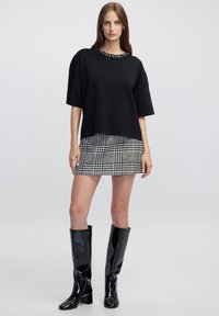 Top negro de manga corta con un escote texturizado, combinado con una falda mini de cuadros en blanco y negro y botas negras brillantes hasta la rodilla.