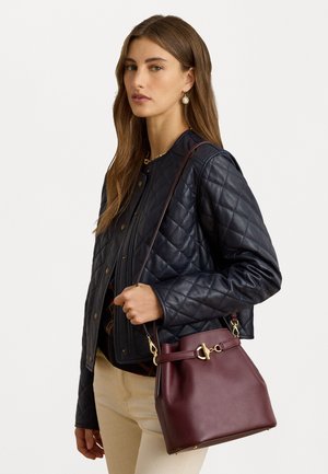 Jakna od mornarice od pamučne kože, uskog kroja, nosi se preko tamne majice. Burgundska torba u obliku kante s zlatnim detaljima, glatke teksture, s naramenicom.