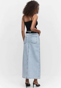 Jupe maxi en denim bleu clair avec une coupe droite, poches arrière et taille mi-haute, associée à une ceinture noire et des talons noirs.