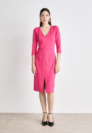 Fuchsia dress with a V-neck, three-quarter sleeves, front slit, and structured fit. Styled with black shoes featuring a knotted detail.