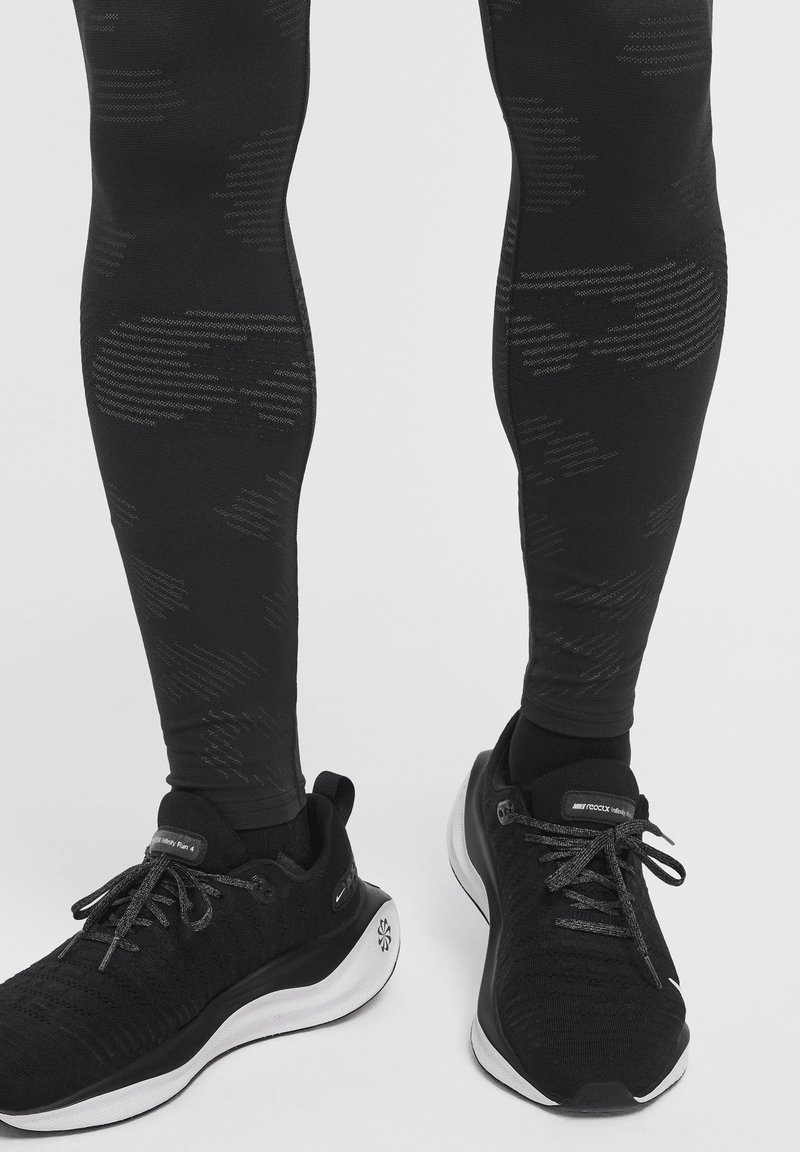 Leggings de sport noirs avec un motif texturé, associés à des chaussures de course noires avec une semelle blanche et des lacets noirs.
