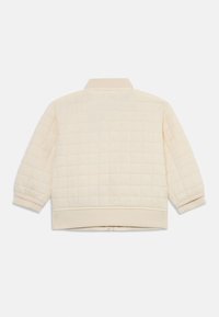 Veste crémée matelassée avec un col, des poignets élastiques et un ourlet. La texture est douce, avec un motif subtil de points de couture carrés.