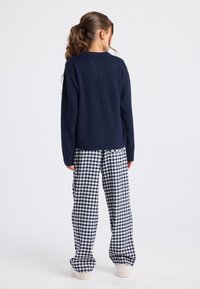 Pull marine à manches longues, associé à un pantalon large à carreaux blancs et marins, et des chaussures beiges à enfiler. Tissu texturé visible.