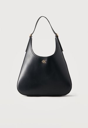 Sac à main en cuir noir avec une seule bandoulière et un logo "cK" doré centré près du haut, présenté sur un fond clair uni.