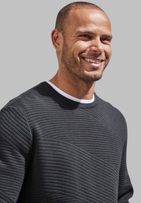 Schwarzer strukturierter Pullover mit einem weißen gerippten Kragen; verfügt über horizontale Linien und geometrische Muster, die in den Stoff eingewebt sind.