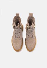Botas de tobillo de ante beige con puntas redondas, diseño con cordones y suelas de goma. Decoradas con herrajes dorados en el costado y un cuello acolchado.