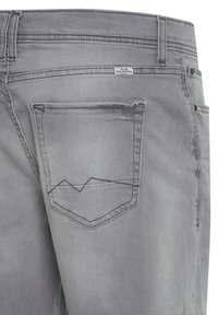Los pantalones de mezclilla grises presentan un bolsillo trasero con un diseño de costura en forma de montaña. La tela tiene una textura suave y una ligera variación en el color.