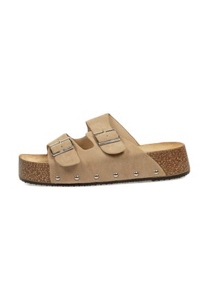 Sandalia deslizante de ante beige con dos correas ajustables y hebillas de plata. Suela de tipo corcho con pequeños studs plateados a lo largo del borde.