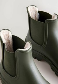 Groene rubberen enkellaarzen met een textiele voering, bontafwerking en gevormde zolen, voorzien van dubbele elastische zijpanelen voor gemakkelijk aantrekken.