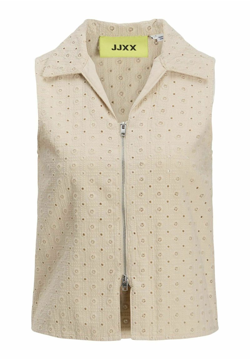 Beige ärmlös topp med dragkedja fram, med ett strukturerat mönster av små blommotiv och en spetsig krage. Varumärkesetikett synlig på insidan.