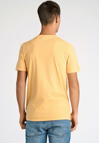 Camiseta corta de color amarillo claro con cuello redondo, textura suave y dobladillo cosido, combinada con unos vaqueros de mezclilla azules.