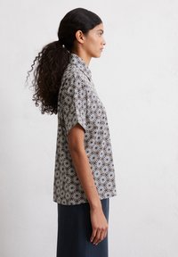 Short-sleeve blouse featuring a black and white geometric floral print, made of lightweight fabric with a relaxed fit and collar.
