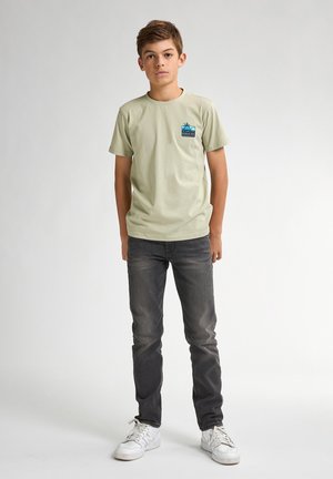 Korte mouw, lichtgroene t-shirt met een blauwe graphic op de borst, gecombineerd met donkergrijze jeans en witte sneakers. Glad materiaal.