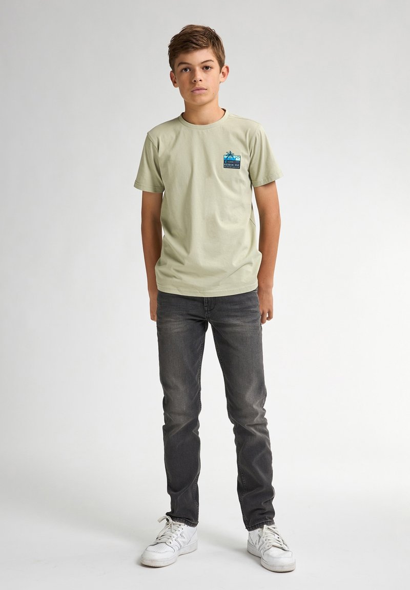 Korte mouw, lichtgroene t-shirt met een blauwe graphic op de borst, gecombineerd met donkergrijze jeans en witte sneakers. Glad materiaal.