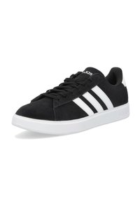 Zapatilla de ante negra con acentos sintéticos blancos y tres rayas blancas. Cuenta con un cuello acolchado y cordones planos negros sobre una suela blanca.