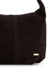 Brun skuldertaske i ruskind med en glat tekstur, logo i guldfarvet metal og en enkel silhuet. Har en central sømdetalje.