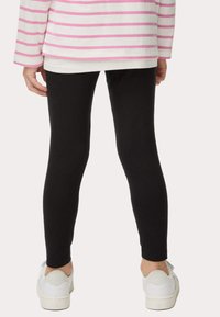 Leggings de algodón negros con un ajuste slim, combinados con zapatillas blancas. La parte superior presenta rayas horizontales rosas y blancas.
