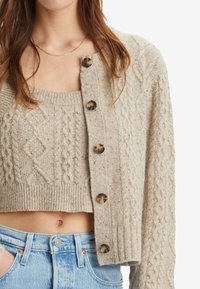 Beige kardigan s kabelkovým úpletem a velkými kulatými knoflíky, s texturovaným povrchem, doplněný o odpovídající top na zkráceném střihu. Materiál směs bavlny.