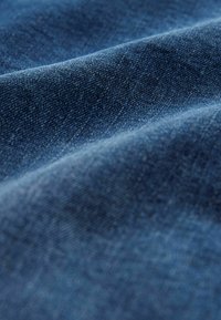 Tamnoplav denim materijal s glatkom teksturom koja prikazuje suptilne varijacije boje, pregibi stvaraju dubinu i dimenziju.