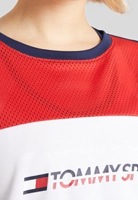 Czerwona i biała sportowa koszulka z siateczkową strukturą, granatowym okrągłym dekoltem i logo "TOMMY". Charakteryzuje się odważnym wzorem z poziomymi blokami kolorów.