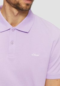 Fioletowa koszulka polo z teksturowanej tkaniny, z klasycznym kołnierzykiem, zapięciem na dwa guziki oraz małym białym logo s.Oliver na piersi.