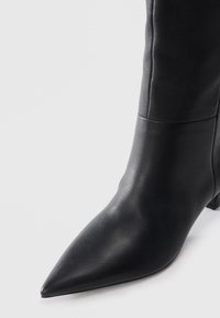 Black leather pointed ankle boot with a smooth texture and a low square heel. Features a clean seam detail on the shaft.