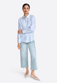 Blauwe en witte gestreepte overhemd met lange mouwen, gecombineerd met lichtgewassen wijde jeans en puntige slingback schoenen.