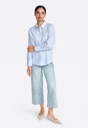 Chemise à rayures bleu et blanche avec des manches longues, associée à un jean large à délavé clair et à des chaussures à bout pointu à talon ouvert.