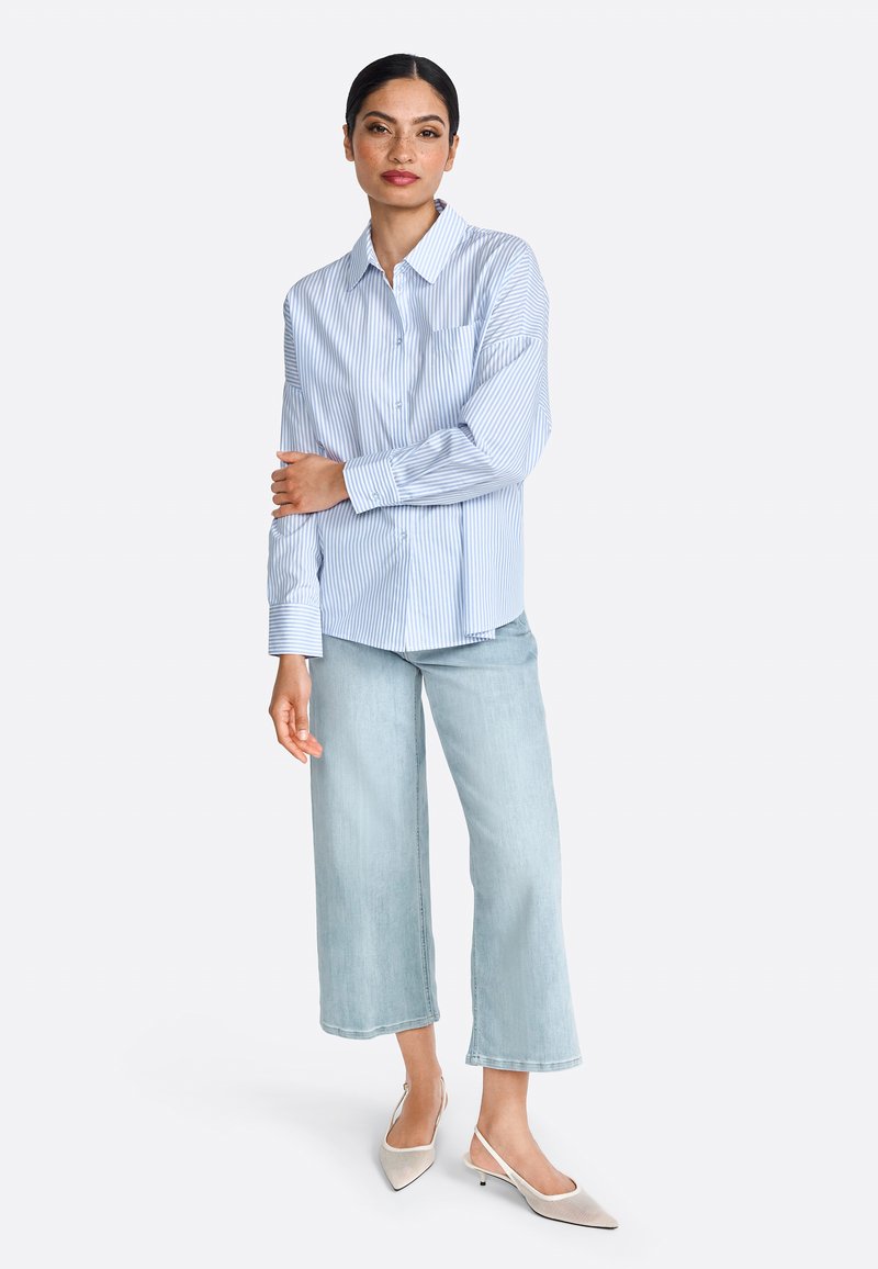 Blauwe en witte gestreepte overhemd met lange mouwen, gecombineerd met lichtgewassen wijde jeans en puntige slingback schoenen.