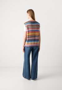 Gestreifter Strickweste in mehreren Farben, mit Rundhalsausschnitt und ärmellosem Design, kombiniert mit weit geschnittenen blauen Jeans und cremefarbenen Schuhen.