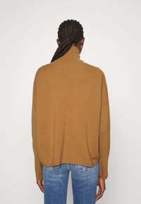 Brązowy, żeberkowany sweter z golfem o luźnym kroju i opadających ramionach, zestawiony z niebieskimi dżinsami. Prosty i nowoczesny design.