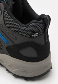 Czarne i szare buty trekkingowe z teksturowaną siateczką, niebieskimi akcentami oraz gumową podeszwą z agresywnym bieżnikiem, oznaczone napisem "OutDry" i "Techlite."