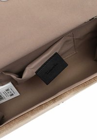 Beige textilní taška uvnitř s hladkou texturou, se černou koženou visačkou. Obsahuje malou kapsu a viditelný štítek s pokyny k údržbě.