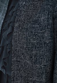 Blisko ujecie czarno-białej teksturowanej tkaniny z warstwą czarnej, falbaniastej organzy częściowo widocznej za nią.