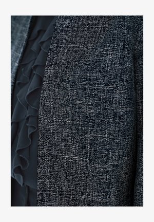 Blisko ujecie czarno-białej teksturowanej tkaniny z warstwą czarnej, falbaniastej organzy częściowo widocznej za nią.