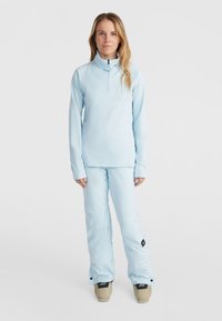 Helle blaue Skijacke mit einem halben Reißverschlusskragen, kombiniert mit passenden Schneehosen. Glattes Material, taillierte Passform und dezentes Logodesign.