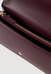 Μπορντό δερμάτινη τσάντα με χρυσό φερμουάρ και αξεσουάρ, διαθέτοντας λεία υφή και απλό σχέδιο, ανοιχτή για να αποκαλύψει την εσωτερική επένδυση.