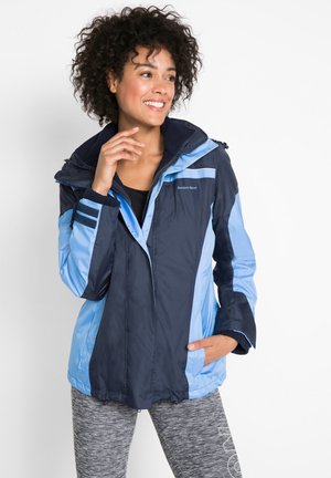 Giacca isolante blu navy e azzurro chiaro con zip frontale e cappuccio. Presenta polsini a costine e branding per sport all'aperto. Texture liscia, resistente all'acqua.